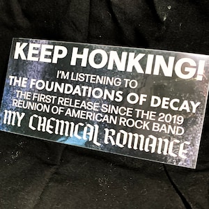 May include: Rectangular sticker with the text "KEEP HONKING!" and "I'M LISTENING TO THE FOUNDATIONS OF DECAY" referencing the My Chemical Romance reunion. The sticker is white with a dark, textured background.