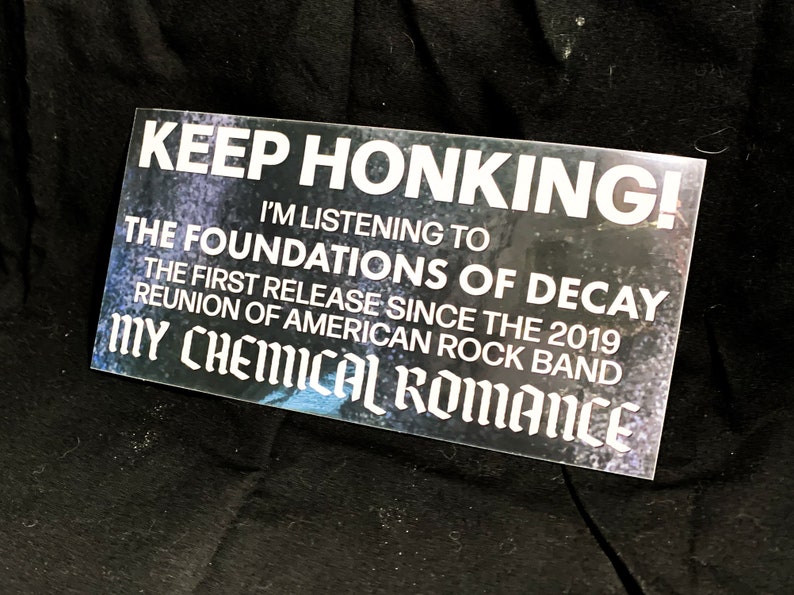 May include: Rectangular sticker with the text "KEEP HONKING!" and "I'M LISTENING TO THE FOUNDATIONS OF DECAY" referencing the My Chemical Romance reunion. The sticker is white with a dark, textured background.