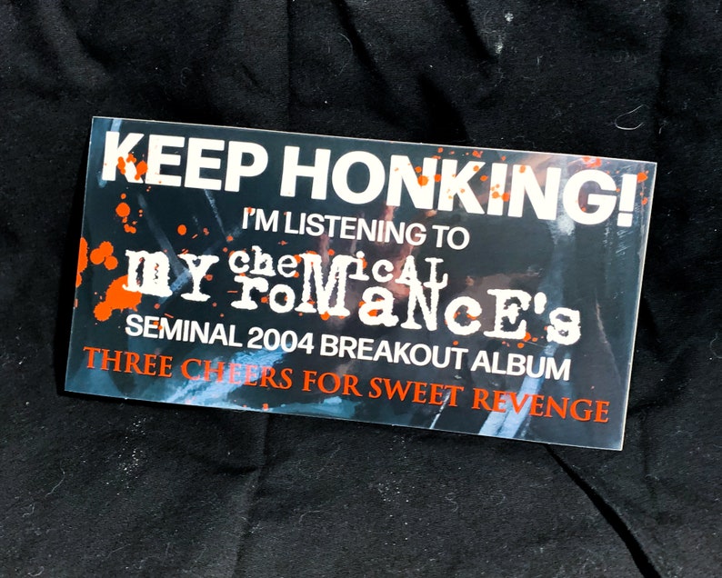May include: Rectangular sticker with the text "KEEP HONKING! I'M LISTENING TO my chemical romance's SEMINAL 2004 BREAKOUT ALBUM THREE CHEERS FOR SWEET REVENGE" in white and orange on a dark background.
