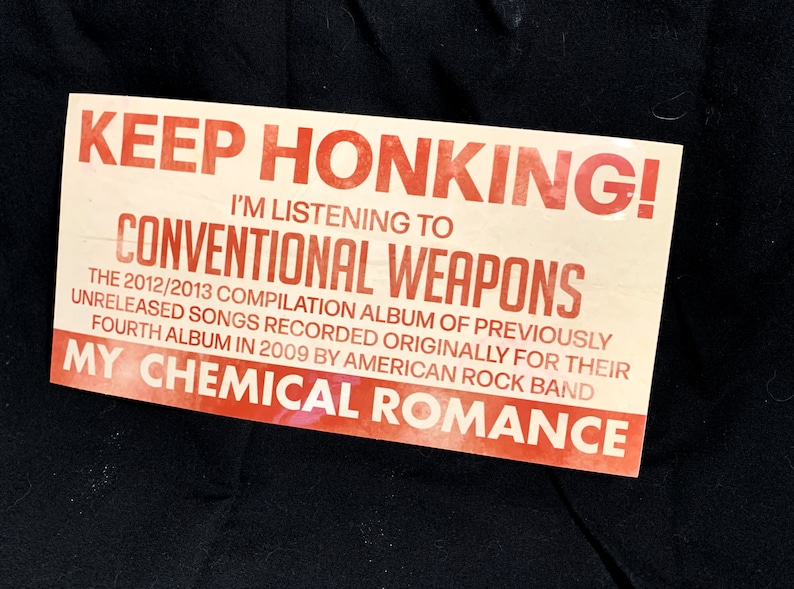May include: A rectangular sticker with the text "KEEP HONKING! I'M LISTENING TO CONVENTIONAL WEAPONS" in red and black. The sticker also mentions "MY CHEMICAL ROMANCE" and details about an album.