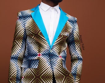 May include: A man wearing a white blazer with a blue and green geometric pattern. The blazer has a blue satin lapel and a single button closure. The man is wearing a white shirt and dark pants. The text "Kwame Tailor" is visible on the right side of the image.