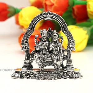 May include: Silver statue of a Hindu deity couple, Lakshmi and Vishnu, standing under an archway. The statue is detailed with intricate carvings and is set on a base with floral designs.
