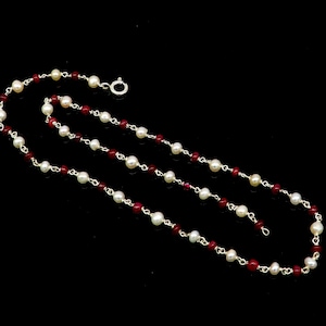May include: A silver chain necklace with alternating white pearls and red gemstone beads.