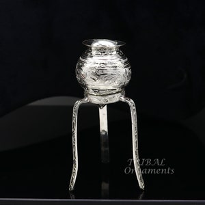 May include: A silver decorative stand with a round top and three legs. The stand is decorated with an intricate floral pattern.