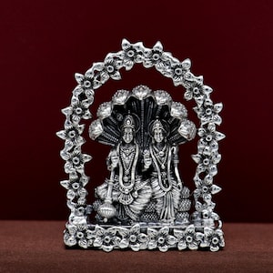 May include: Silver statue of a Hindu deity couple, seated on a throne with a snake hood, framed by a decorative floral arch.