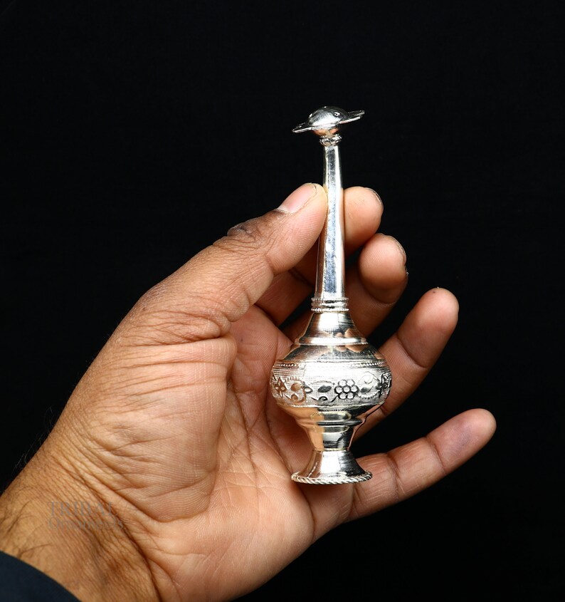 May include: A silver perfume bottle with intricate floral designs. The bottle has a long, slender neck and a small, round top.