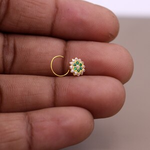 May include: A gold nose ring with a circular design featuring green and white stones.