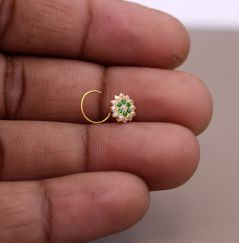 May include: A gold nose ring with a circular design featuring green and white stones.