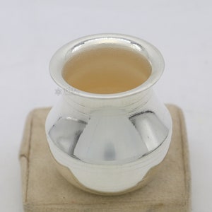 May include: A silver, round, pot-shaped container with a wide, flat rim. The container is polished and shiny, reflecting the light.