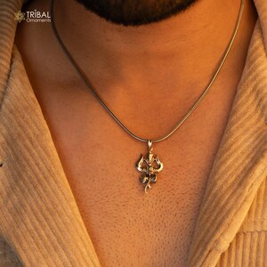 May include: A silver chain necklace with a silver pendant featuring a detailed design of a trident, a three-pronged spear, a symbol of the Hindu god Shiva.