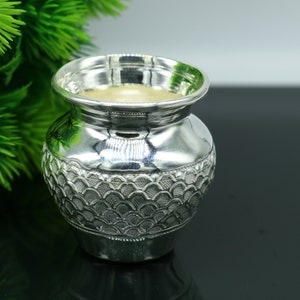 May include: A silver, decorative, ceremonial pot with a textured, scalloped design. The pot is made of polished silver and has a round, wide mouth.