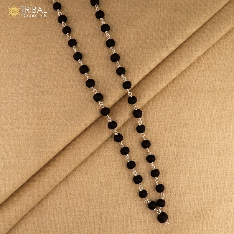 May include: A black beaded necklace with silver-toned chain links. The necklace features round, matte black beads. The Tribal Ornaments logo is in the upper left corner.
