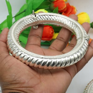 May include: A silver bangle bracelet with a textured design. The bracelet is open and has a hinged clasp.