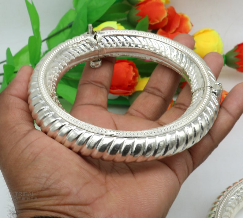 May include: A silver bangle bracelet with a textured design. The bracelet is open and has a hinged clasp.