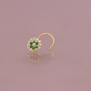 May include: A gold nose ring with a circular design featuring white and green gemstones.