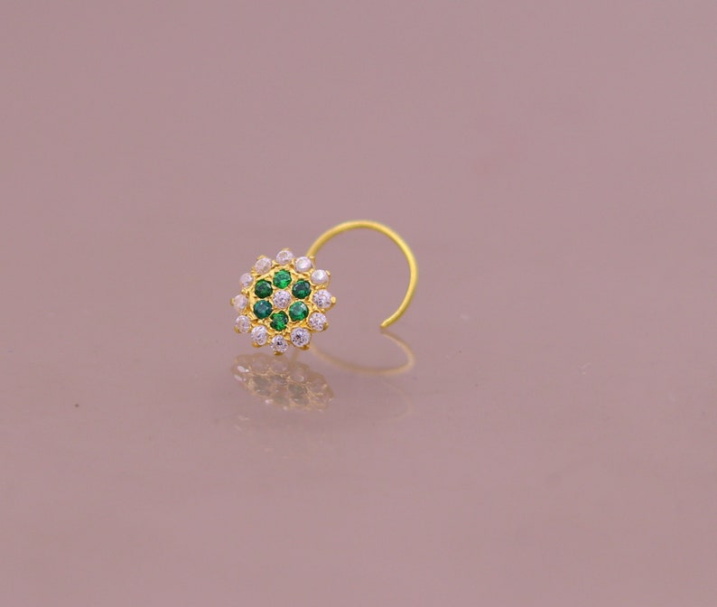May include: A gold nose ring with a circular design featuring white and green gemstones.