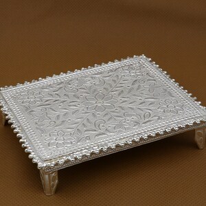 Puede incluir: Una bandeja de plata con un diseño floral y cuatro patas. La bandeja está hecha de metal y tiene un acabado brillante.