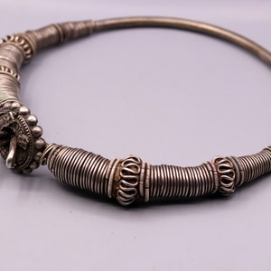 May include: A silver necklace with a unique design featuring multiple coiled wire rings. The necklace has a clasp closure and is decorated with small, round beads.