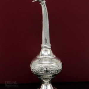 May include: A silver decorative bottle with an ornate design and a long spout. The bottle has a round base and a lid with a star-shaped design.