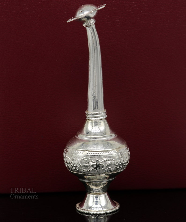 May include: A silver decorative bottle with an ornate design and a long spout. The bottle has a round base and a lid with a star-shaped design.