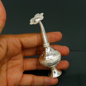 May include: A silver flower-shaped perfume bottle with an ornate design. The bottle has a long, slender neck and a small, round base.