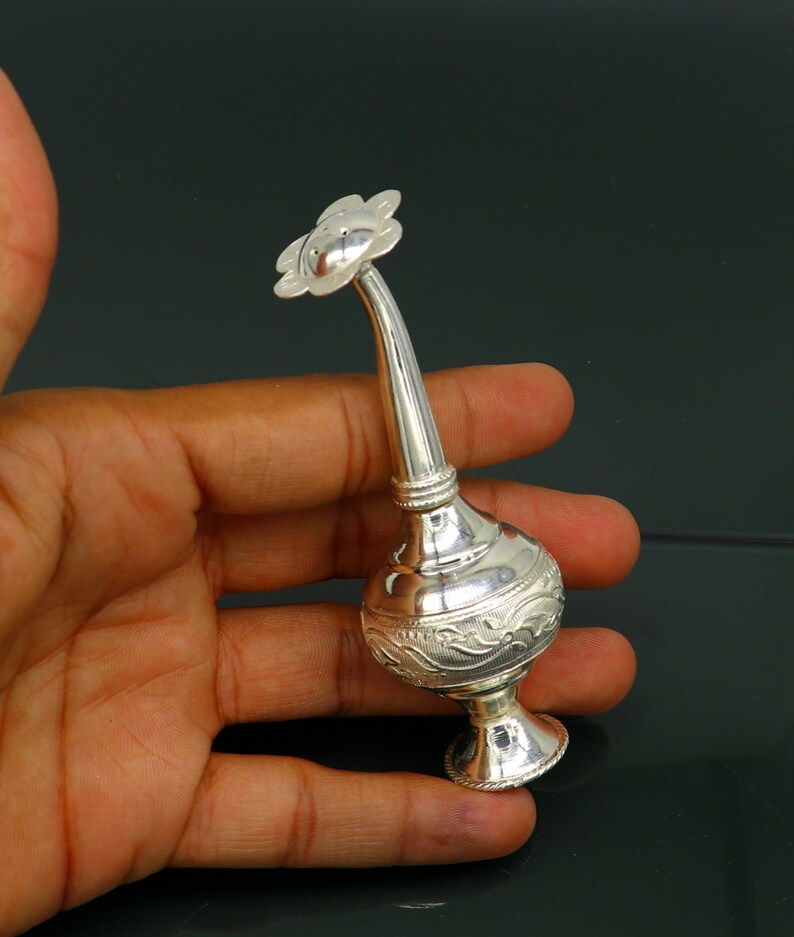 May include: A silver flower-shaped perfume bottle with an ornate design. The bottle has a long, slender neck and a small, round base.