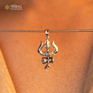 May include: Silver pendant necklace featuring a detailed design of a trident and a small drum, a symbol of the Hindu god Shiva.