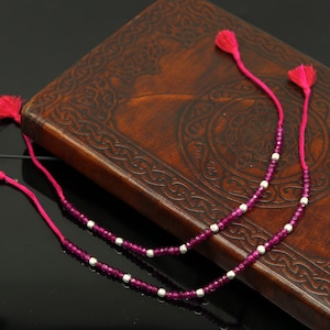 Puede incluir: Dos pulseras de cuentas rosadas y plateadas con borlas sobre un fondo de cuero marrón.