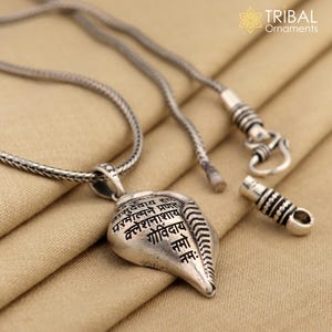 Op de afbeelding: Zilveren ketting met een schelp hanger met Sanskriet tekst. De ketting heeft een gevlochten ketting en een schuifsluiting.