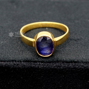May include: A gold ring featuring a blue oval gemstone. The ring is displayed on a black velvet background.