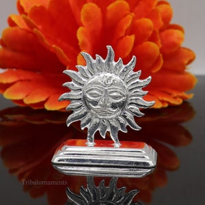 May include: Silver Surya Deva, the Hindu Sun God, depicted as a stylised sun with a face. The deity is standing on a square base.
