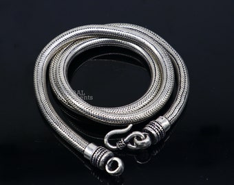 Può includere: Una collana a catena di serpente d'argento con chiusura a moschettone. La catena è realizzata con piccoli anelli intrecciati che creano un aspetto liscio e fluido.