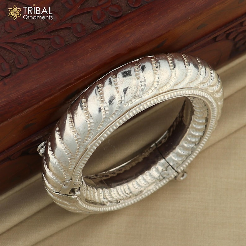 May include: A silver bangle bracelet with a decorative, textured design. The bracelet is open and has a hinged clasp.