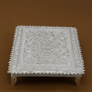 Puede incluir: Una bandeja decorativa de plata con un intrincado diseño floral y un borde de cuentas. La bandeja tiene cuatro patas y está hecha de metal.