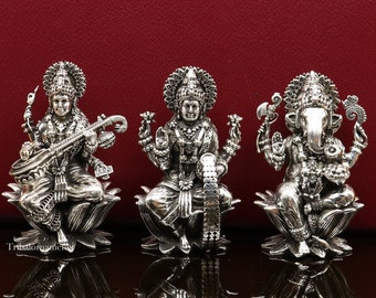 Op de afbeelding: Drie zilveren beelden van hindoeïstische goden: Saraswati, Lakshmi en Ganesha. Elk beeld zit op een lotusbloem en is ingewikkeld gedetailleerd.
