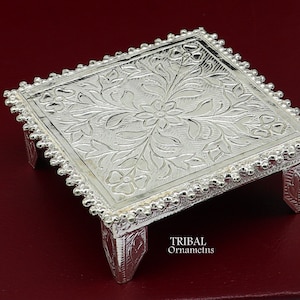 Puede incluir: Una bandeja cuadrada de plata con un intrincado diseño floral y cuatro patas. La bandeja tiene un borde de cuentas y está hecha en un estilo tradicional.