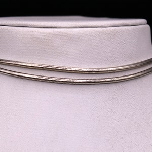 May include: A silver snake chain necklace displayed on a white mannequin bust. The chain is double-layered and has a smooth, polished finish.