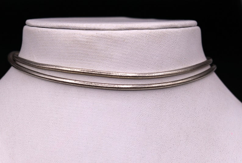 May include: A silver snake chain necklace displayed on a white mannequin bust. The chain is double-layered and has a smooth, polished finish.
