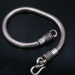 K&ouml;nnte beinhalten: Ein silbernes Schlangenkettenarmband mit einem Hakenverschluss. Das Armband ist aus Sterlingsilber gefertigt und hat eine polierte Oberfl&auml;che.
