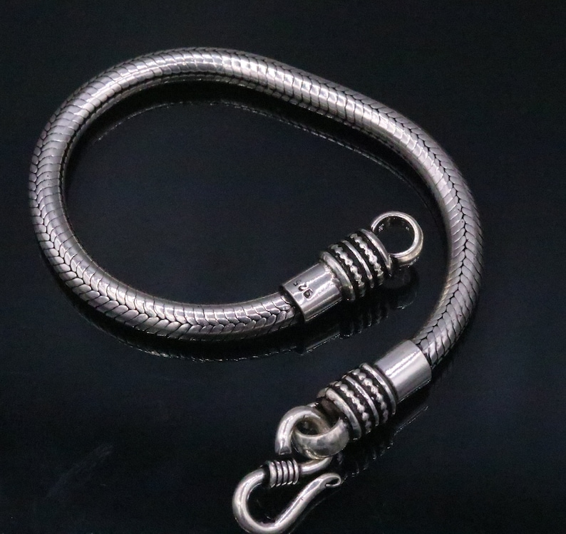 K&ouml;nnte beinhalten: Ein silbernes Schlangenkettenarmband mit einem Hakenverschluss. Das Armband ist aus Sterlingsilber gefertigt und hat eine polierte Oberfl&auml;che.