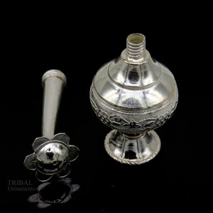 May include: Silver perfume bottle with a floral design and a separate nozzle. The bottle has a round body and a small, round base.