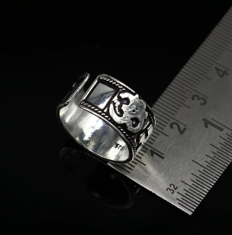 May include: Silver ring with an intricate design featuring a square shape and a floral pattern. The ring is marked with the number "925" indicating it is made of sterling silver.