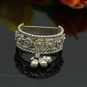 May include: Silver bracelet with a decorative design of flowers and bells. The bracelet is made of silver and has a delicate, intricate design.