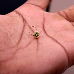 May include: A gold nose ring with a circular design featuring white and green gemstones.