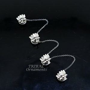 Könnte beinhalten: Vier silberne Lotusblüten-Anhänger, die durch eine silberne Kette verbunden sind. Die Anhänger sind detailliert und haben ein dreidimensionales Design. Die Kette ist zart und hat ein schlichtes Design.