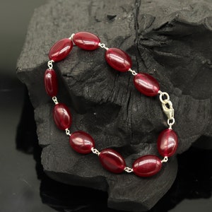 Puede incluir: Un brazalete de piedras preciosas rojas con eslabones de plata. El brazalete está hecho de piedras preciosas rojas de forma ovalada y eslabones de plata.