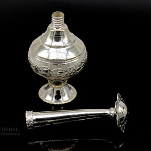 May include: A silver, ornate, decorative bottle with a floral design and a separate nozzle. The bottle has a round body and a flared base. The nozzle is long and slender with a decorative top.
