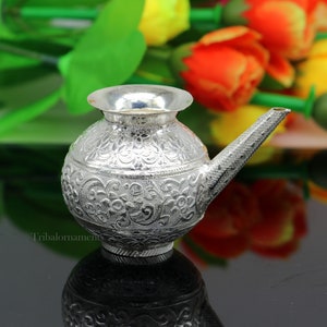 May include: A silver water pot with a floral design. The pot has a spout and a round body. The pot is sitting on a black surface.