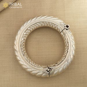 May include: Silver bangle bracelet with intricate, detailed designs. The bracelet is hinged and opens for easy wear.