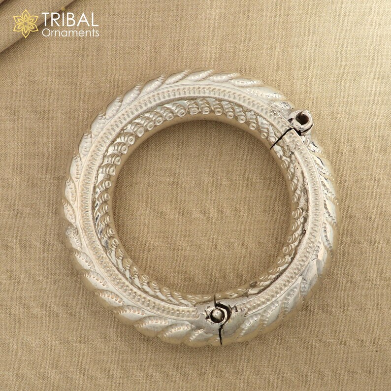 May include: Silver bangle bracelet with intricate, detailed designs. The bracelet is hinged and opens for easy wear.
